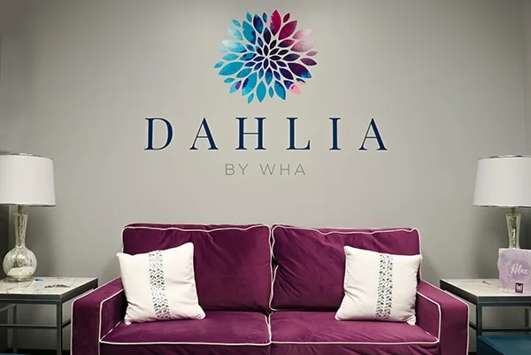 The Dahlia lounge: a plum velvet sofa beneath the dahlia logo on the wall