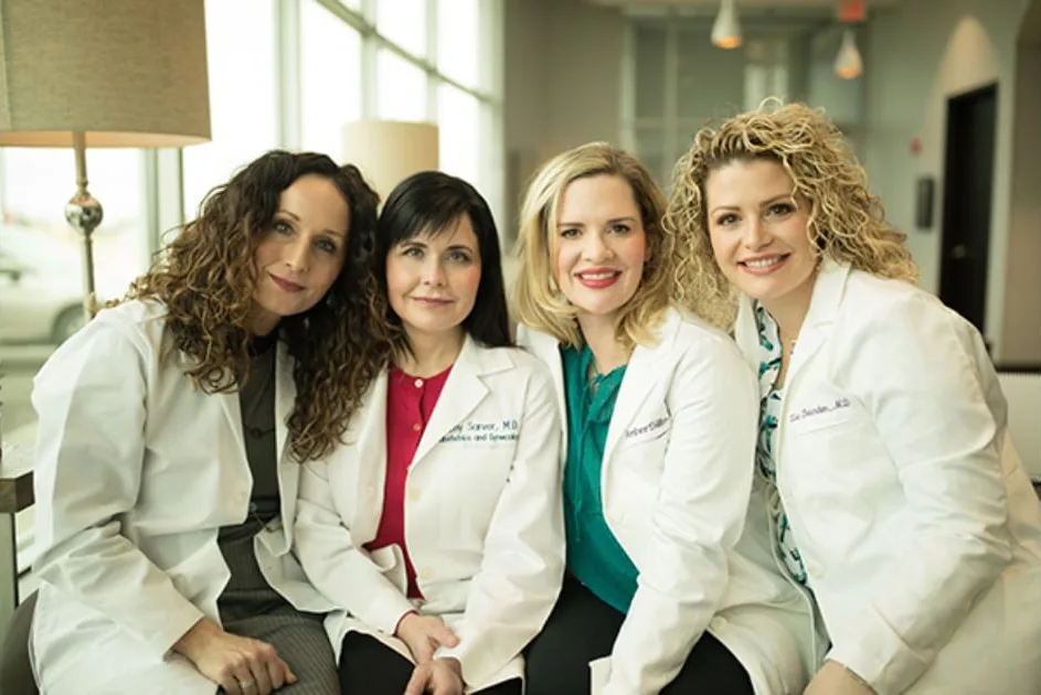 Jamie Gallagher, PAC, and Drs. Amy Sarver, Amber Sills and Lisa Bearden in white coats, seated together in the practice